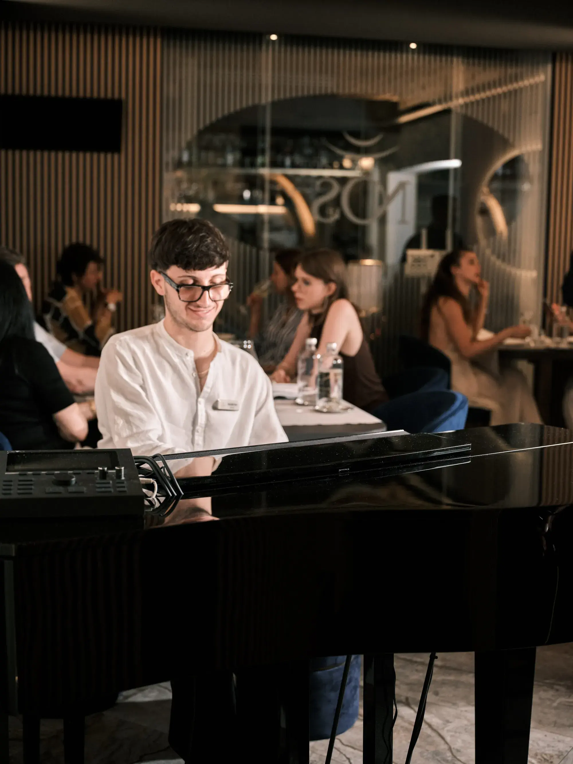 Martin al pianoforte a coda di NOS, la sala che cena alle spalle e l'insegna NOS sul fondo