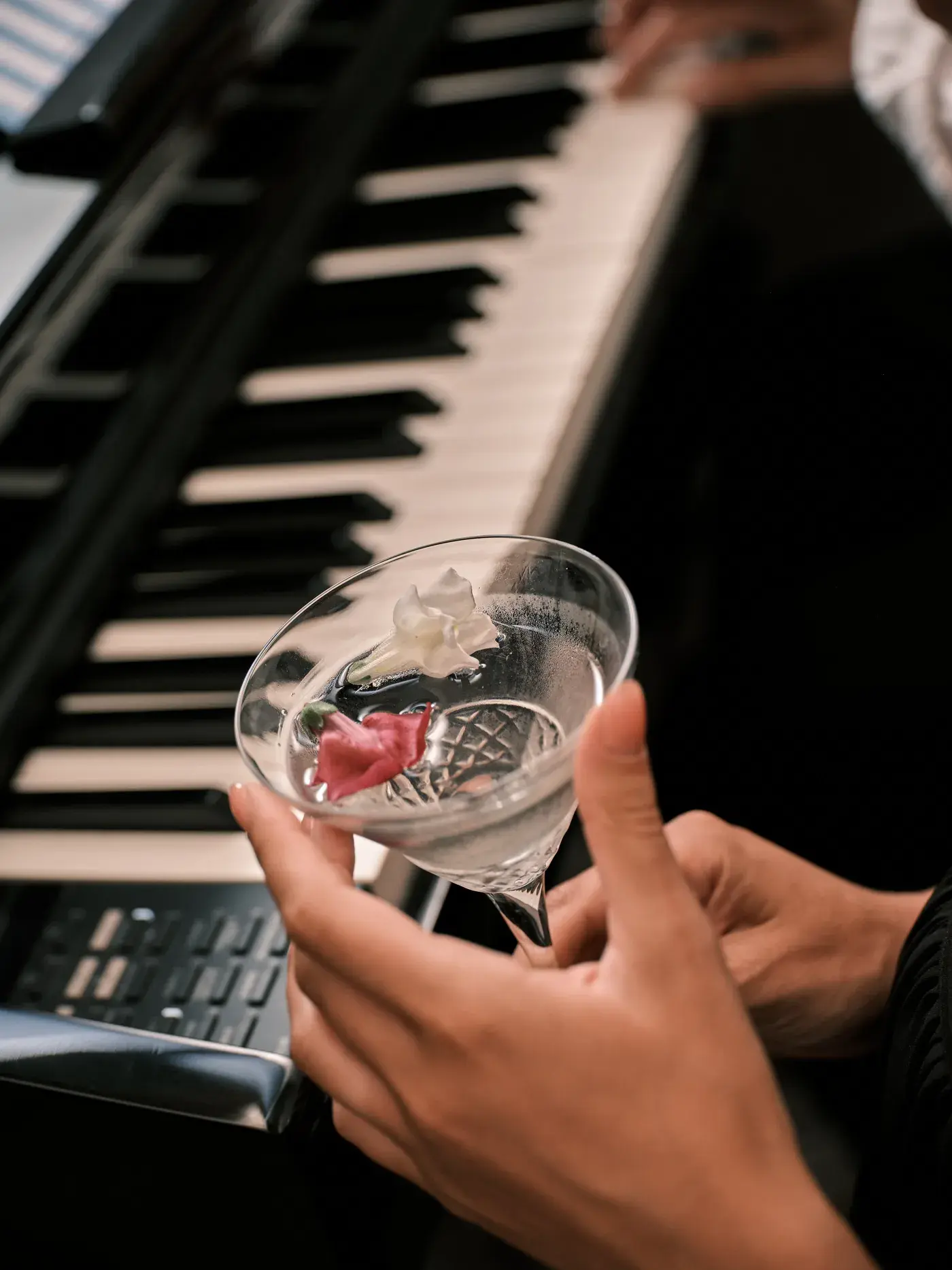 Un cocktail tenuto in mano davanti ai tasti del pianoforte di NOS