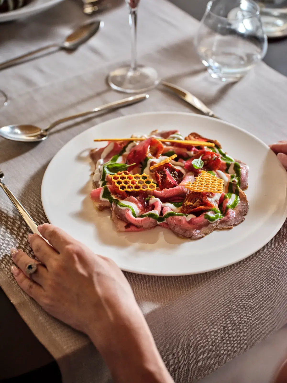 Roastbeef alla Pugliese affettato sottile con pomodorini confit, gel di prezzemolo e cialde a nido d'ape, servito a tavola apparecchiata