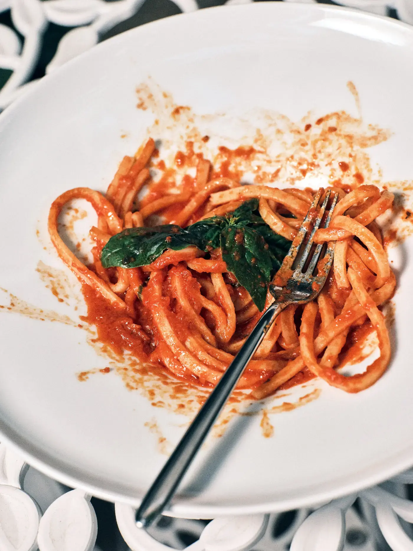 Un piatto di spaghetti al pomodoro con basilico, mangiato a metà, sul tavolo di ferro bianco del giardino di NOS