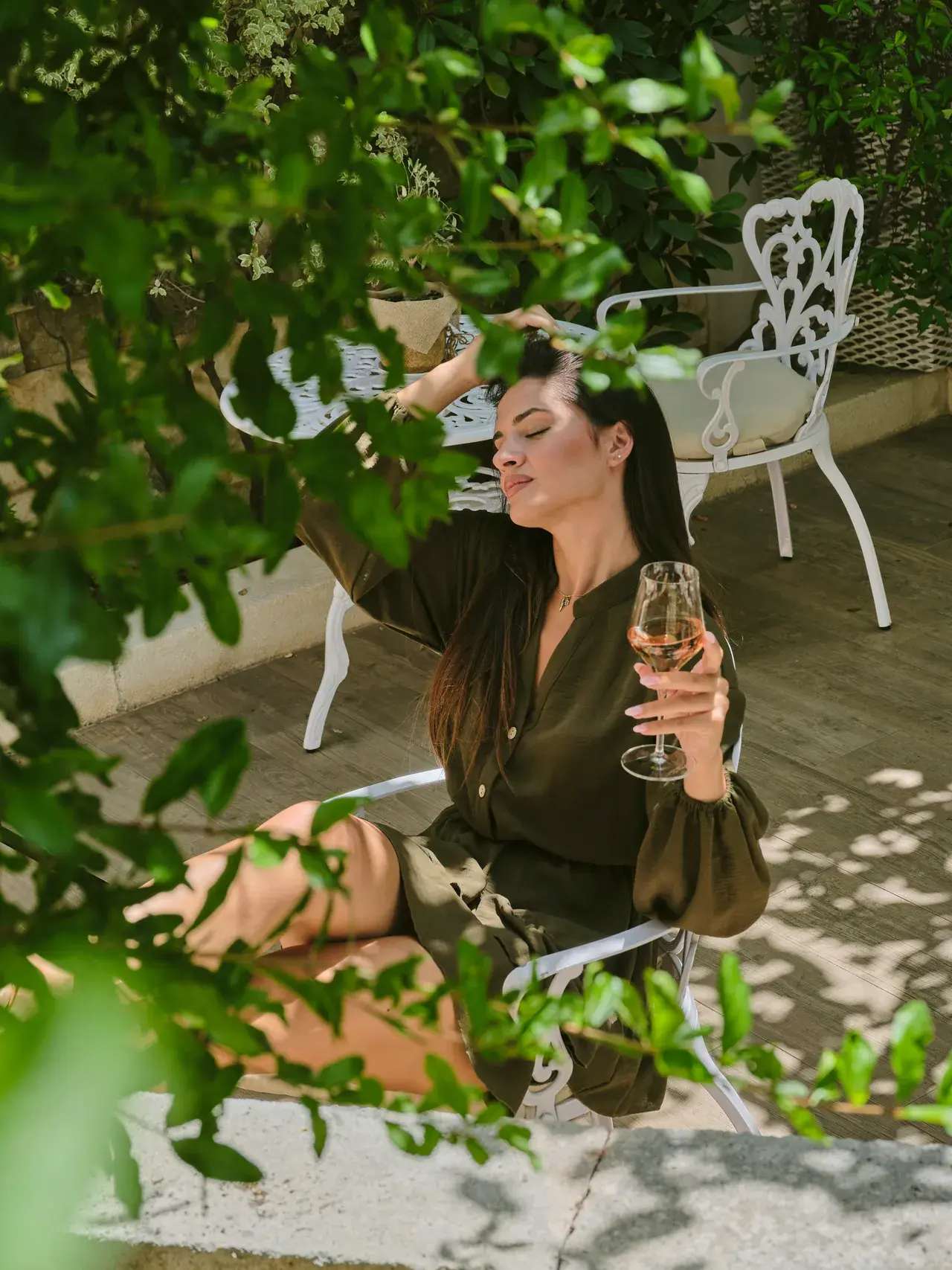 Donna in abito kaki seduta all'aperto tra la vegetazione con calice di vino bianco, relax a Palazzo Scotto
