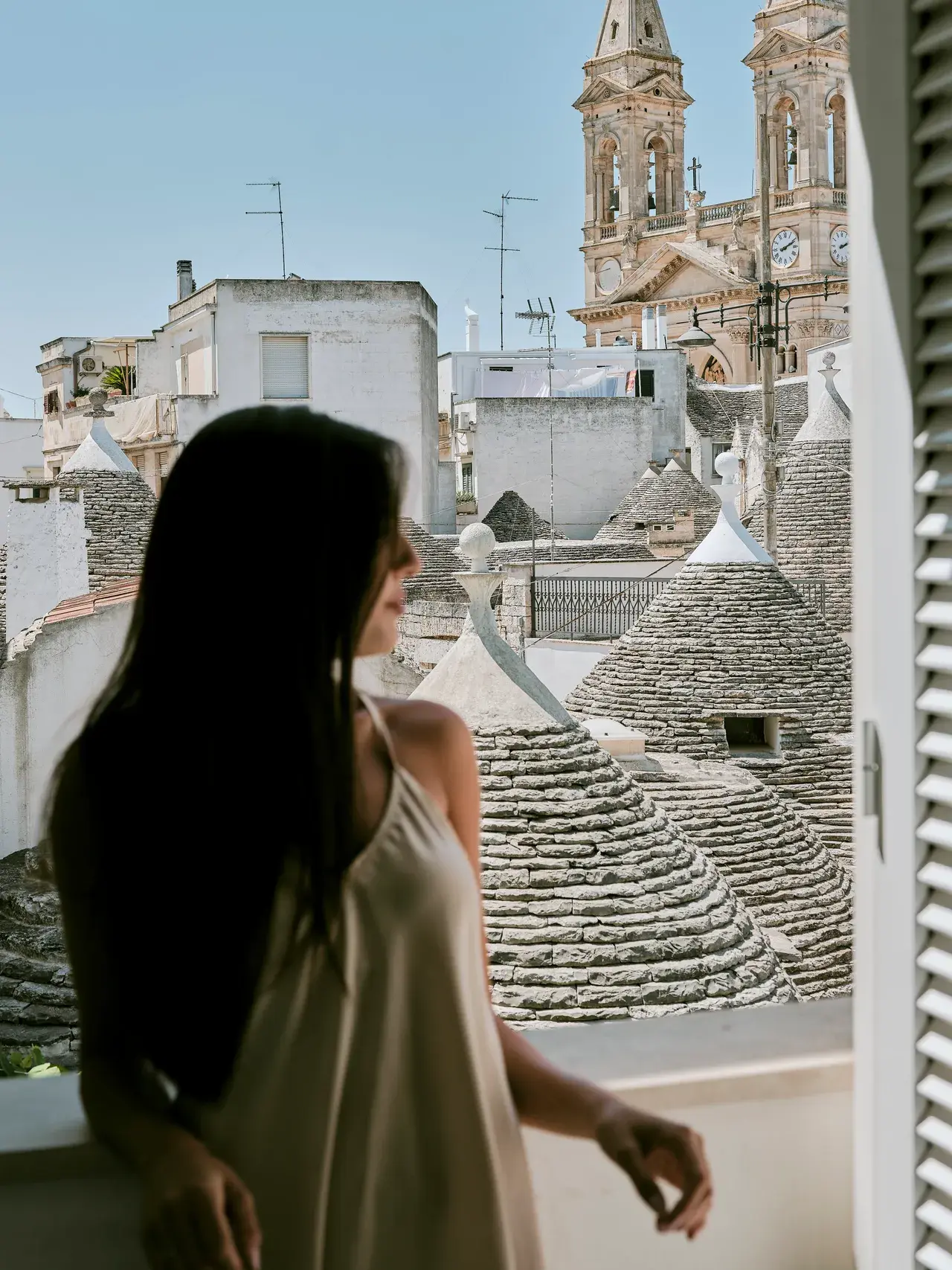 Donna di spalle osserva il panorama dei trulli di Alberobello dalla finestra di Palazzo Scotto, luce estiva naturale