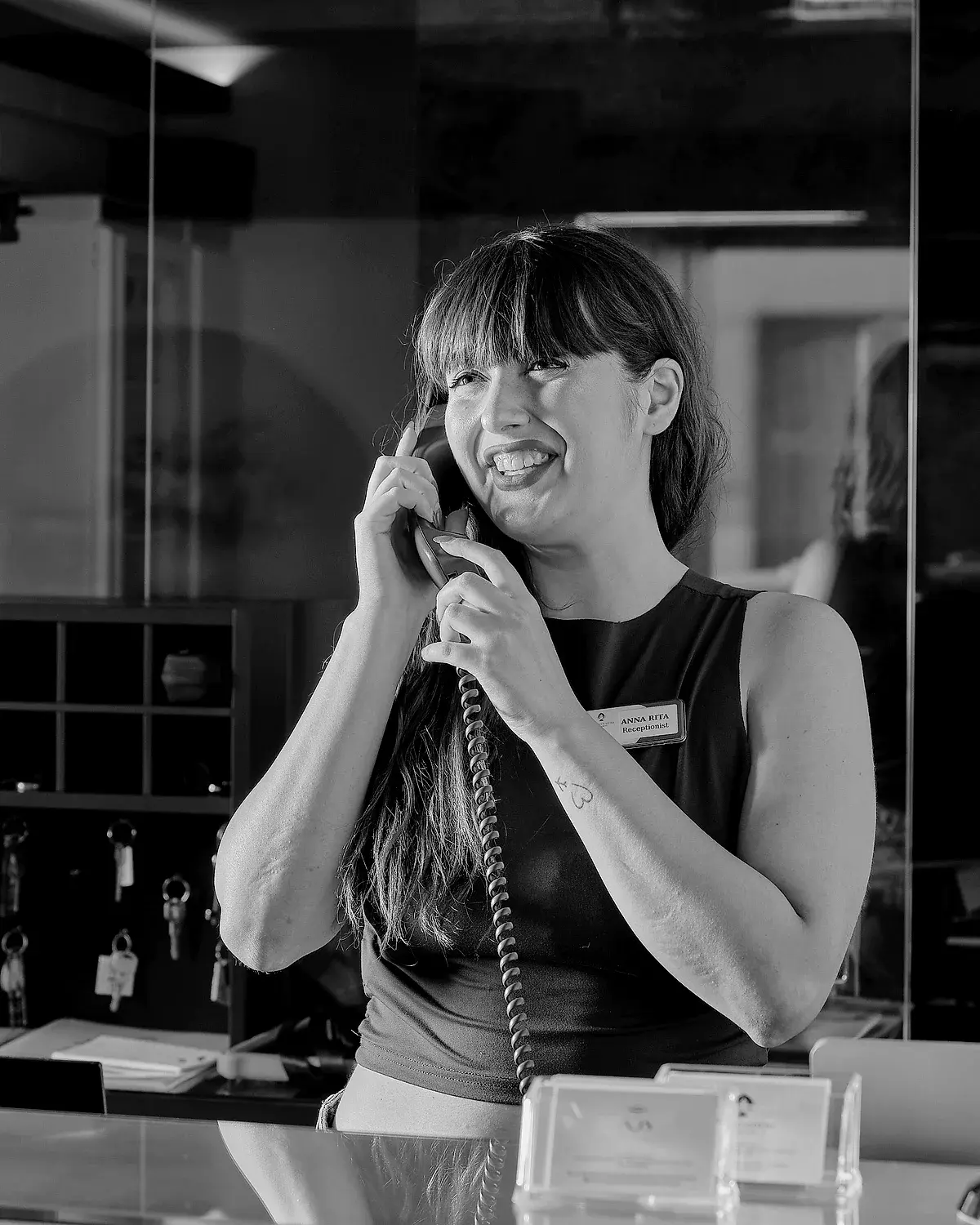 Annarita sorride al banco dell'accoglienza, con la cornetta del telefono in mano.