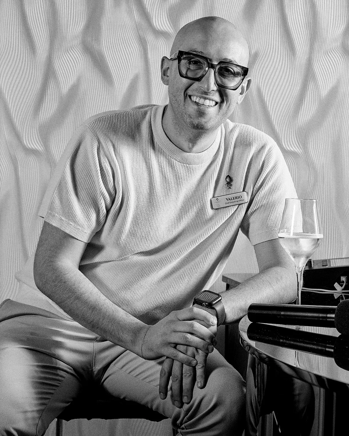 Valerio, in bianco e nero, seduto accanto al pianoforte di NOS con un calice di vino